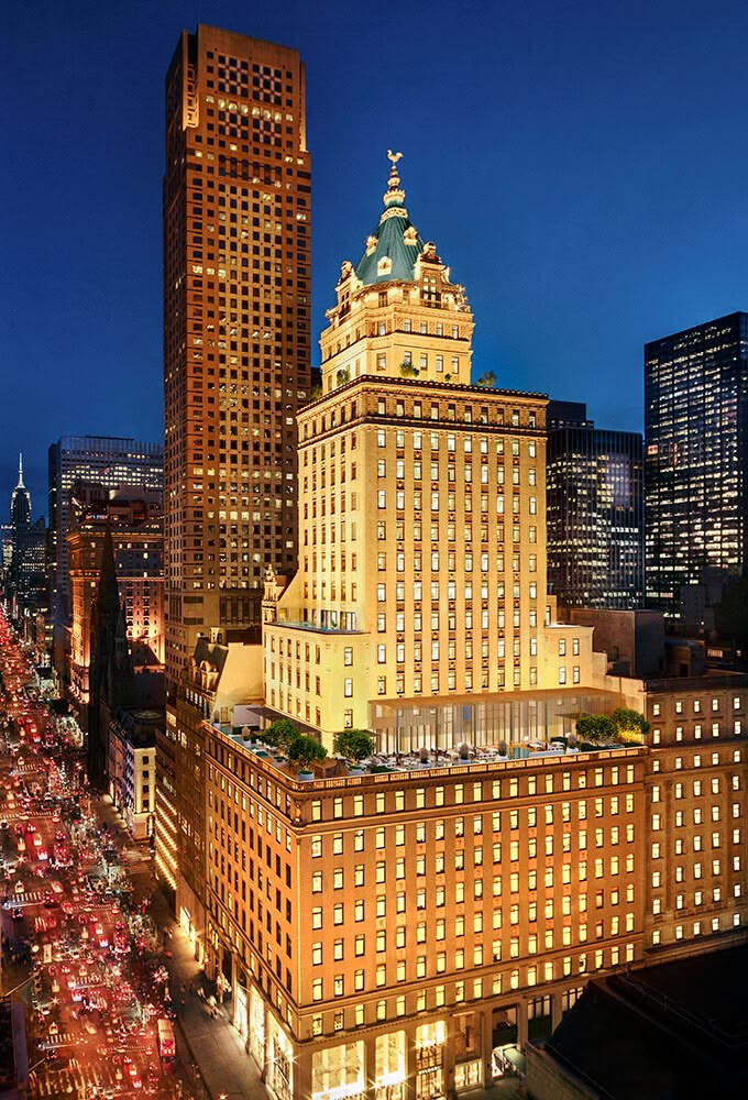 The landmarked King Cole tower rising above Fifth Avenue at blue hour, city traffic streaking below, an icon of long-horizon luxury real estate and hospitality